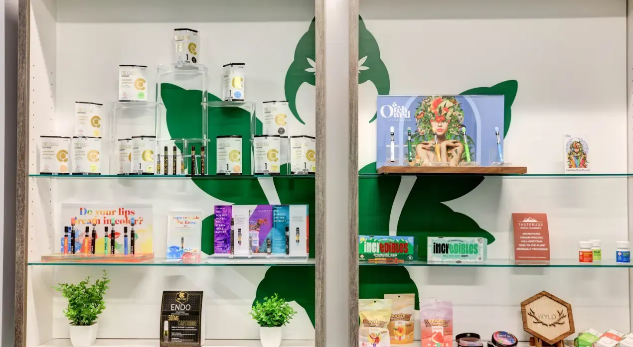 Shelves of vape cartridges, edibles and accessories in front of a green leaf mural on the Emerald Fields sales floor.